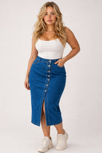 A woman modeling a blue denim midi skirt with a front button placket and side slit, paired with a white tank top and white sneakers, against a plain light gray studio background.