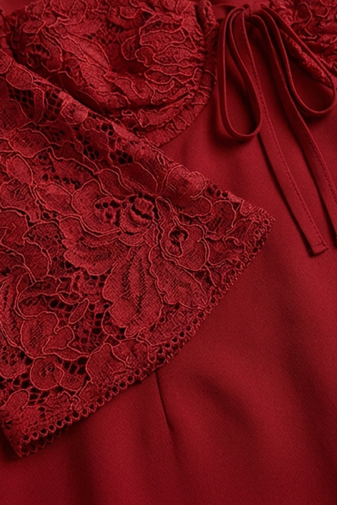 Close-up of a deep red dress featuring a floral lace overlay on the bodice and sleeve, with a matching fabric tie detail and smooth red satin-like fabric underneath.