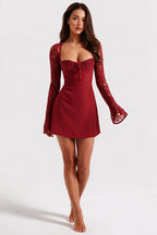 A woman modeling a short burgundy dress with long lace sleeves, a sweetheart neckline, and a sweetheart bust detail, set against a plain light gray studio background.