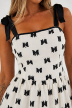 Close-up of a woman wearing a white dress with a black bow print and black ribbon shoulder straps.
