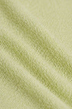 A close-up of a light sage green textured fabric, showing the soft terry cloth or boucle weave with gentle folds.