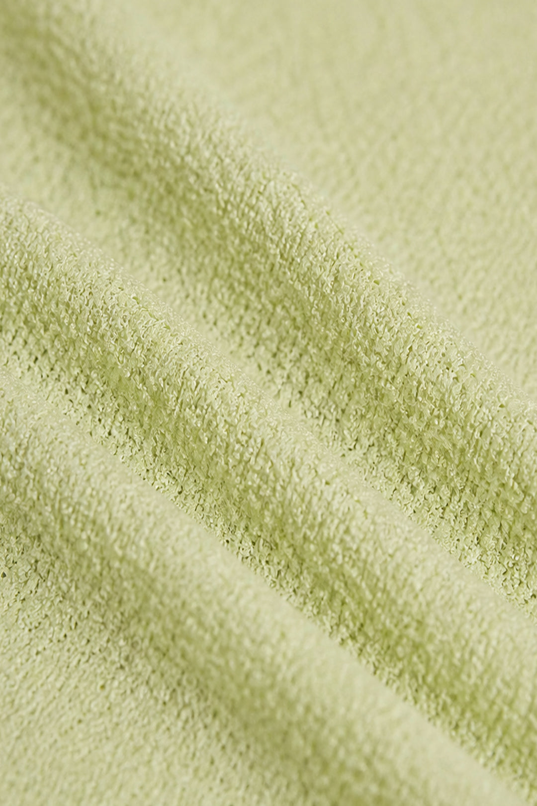 A close-up of a light sage green textured fabric, showing the soft terry cloth or boucle weave with gentle folds.