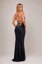 A woman modeling a floor-length black satin gown from the back, showing a strappy open back and a fitted silhouette, against a plain light gray studio background.