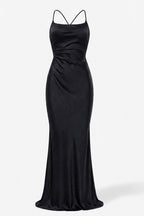 A floor-length black satin gown with thin crisscross spaghetti straps, a fitted bodice, and a draped waist detail, shown against a plain white studio background.