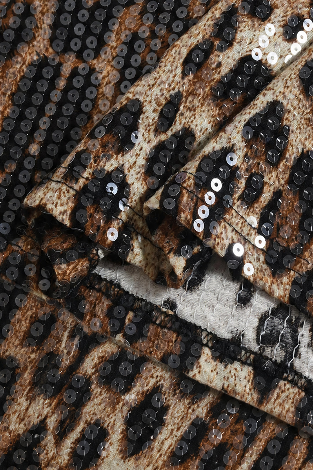 Close-up of leopard-print sequin fabric with black, brown, and beige tones and reflective silver sequins layered over a textured base.