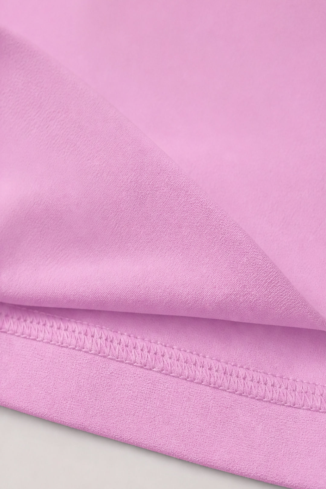 A close-up of light pink fabric with a folded hem showing fine knit texture and stitched edge.