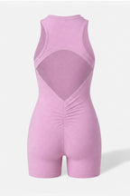 A sleeveless light pink one-piece romper with a large open back design and gathered ruching at the center front, shown on a light gray background.