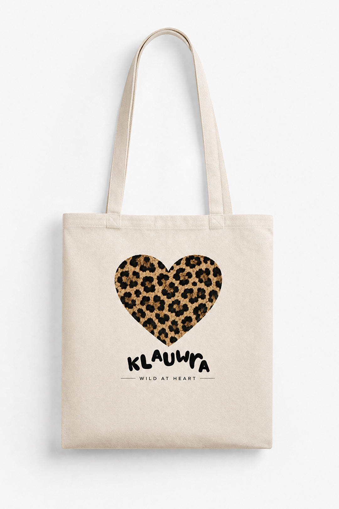 A natural canvas tote bag with a leopard print heart graphic and the text 'KLAUWRA WILD AT HEART' printed on the front, shown against a plain white background.