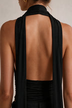 Close-up back view of a woman wearing a black halter-style top with a wide open back and long draped straps.
