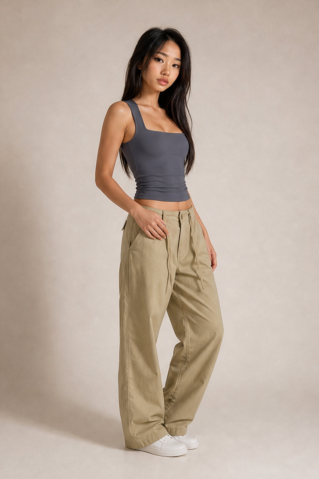 A woman modeling a dark gray ribbed tank top and beige wide-leg cargo pants against a neutral beige studio backdrop.