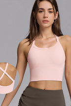 A woman wearing a light pink ribbed halter crop top and dark olive green bottoms, shown against a solid gray studio background. A circular inset on the left highlights the back straps of the pink top.