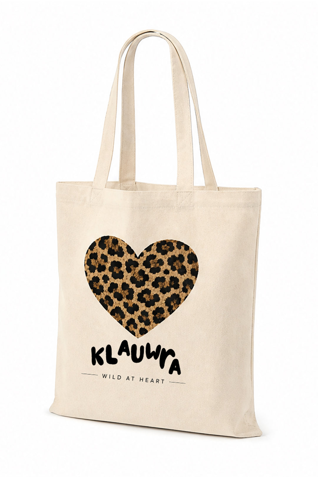 A natural canvas tote bag with a leopard print heart graphic and the text 'KLAUWRA WILD AT HEART' printed on the front, set against a plain white background.