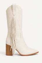 An off-white leather cowboy boot with a pointed toe, a stacked brown block heel, and a long fringe detail on the side, shown against a plain white background.