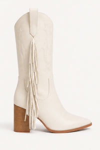 An off-white leather cowboy boot with a pointed toe, a stacked brown block heel, and a long fringe detail on the side, shown against a plain white background.