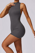 A woman modeling a dark gray sleeveless bodycon mini dress with a mock neck and side cutouts, shown against a light gray studio background.