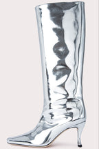 A metallic silver knee-high boot with a pointed toe and slim high heel, shown against a solid light beige background.