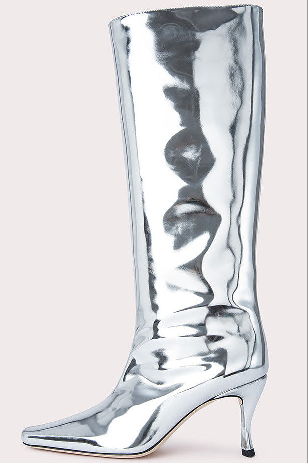 A metallic silver knee-high boot with a pointed toe and slim high heel, shown against a solid light beige background.