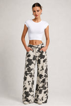 A woman modeling a white short-sleeve crop top and black-and-white cow-print wide-leg pants against a light gray studio background.