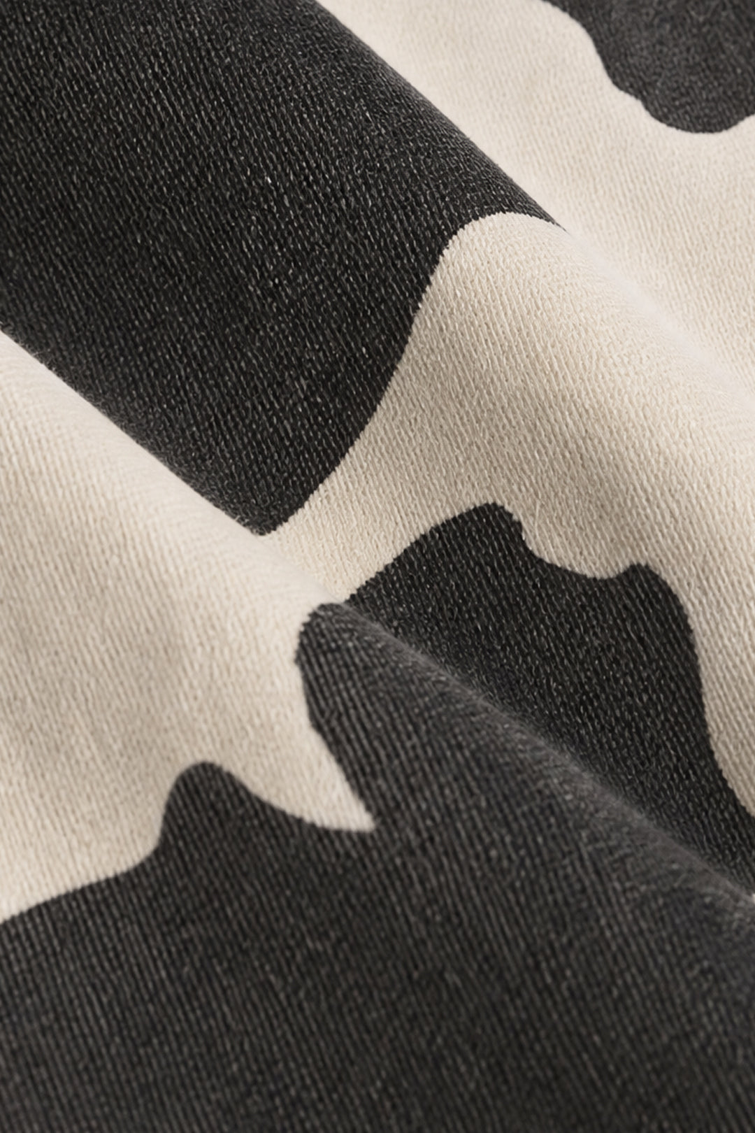 Close-up of a black and off-white cow-print fabric texture with soft folds.