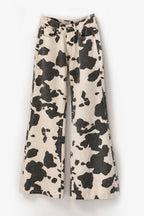 Wide-leg pants featuring a black and beige cow print pattern, displayed against a clean white background.