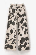 Wide-leg pants featuring a bold black and cream cow print pattern, displayed flat against a clean white background.