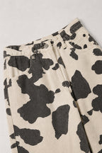 Close-up of a pair of wide-leg jeans featuring a black and off-white cow print pattern, laid flat on a light gray background.
