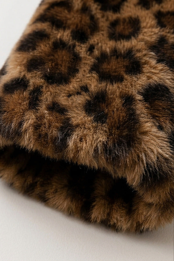 A close-up of a folded faux fur fabric with a brown and black leopard print pattern on a light background.
