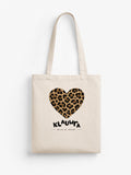 A cream canvas tote bag with two shoulder straps, featuring a leopard-print heart graphic and the text 'KLAUWRA WILD AT HEART' printed on the front, set against a plain white background.