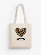 A cream canvas tote bag with two shoulder straps, featuring a leopard-print heart graphic and the text 'KLAUWRA WILD AT HEART' printed on the front, set against a plain white background.