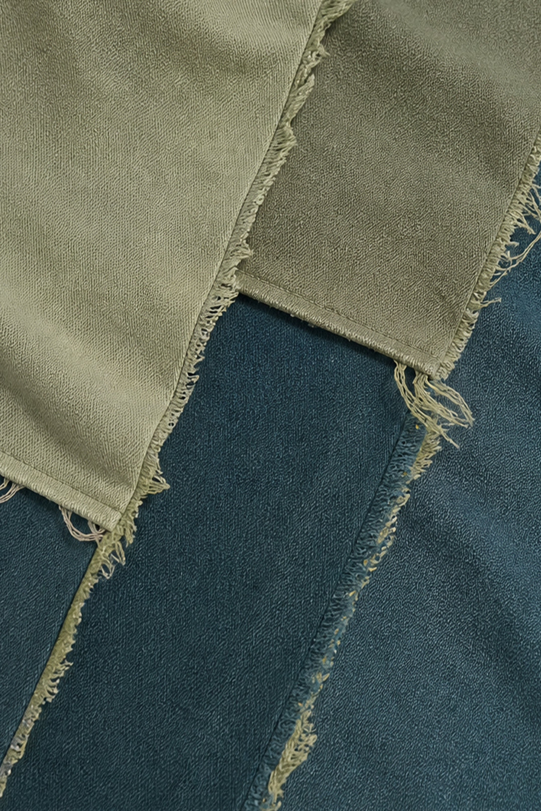A close-up of a patchwork fabric garment featuring a light olive-beige linen-like section with raw frayed edges layered over a dark blue denim section.