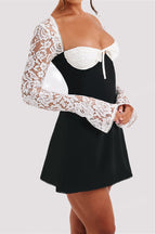 A woman wearing a black and white mini dress with a white lace long-sleeve overlay and a white sweetheart neckline with a bow.