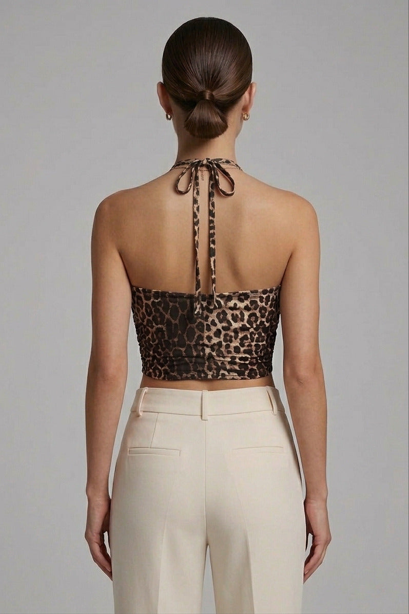 A woman shown from the back wearing a leopard-print halter crop top and cream-colored trousers, set against a solid gray studio background.