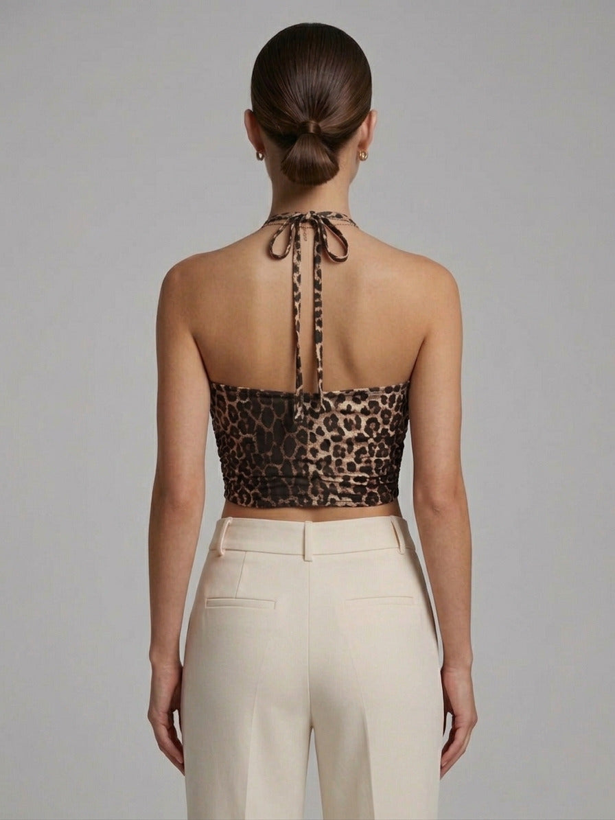 Woman wearing a leopard print halter top and beige pants against a gray background