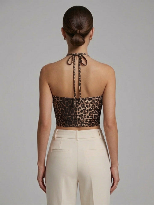 Woman wearing a leopard print halter top and beige pants against a gray background