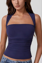 A woman wearing a dark purple halter-style crop top with ruched detailing at the waist, paired with blue jeans, against a light gray background.