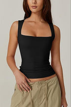 Woman wearing a black tank top and beige pants against a neutral background