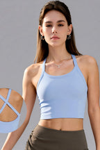 A woman modeling a light blue athletic crop top with a racerback design, shown against a solid gray background. A circular inset on the left highlights the back cutout details of the top.