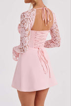 A model shown from the back wearing a light pink mini dress with long lace sleeves, a lace-up open back, and a flared skirt.