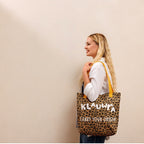 A woman with blonde hair stands in profile against a plain beige wall, carrying a leopard-print tote bag with yellow straps. The bag has the brand name 'KLAUWRA' and the phrase 'CARRY YOUR ORIGIN' printed on it in white.