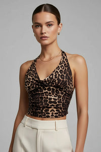 A woman modeling a brown and black leopard print halter crop top paired with cream-colored trousers, set against a solid gray studio background.